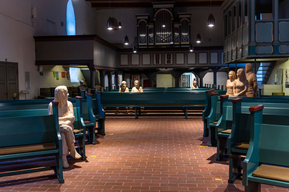 Lebensgroße Holzfiguren sitzen in den Kirchenbänken 